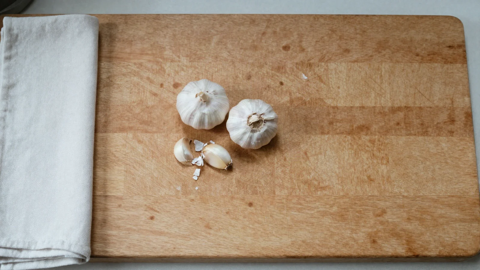 Two garlic bulbs and a few cloves on a wooden cutting board.