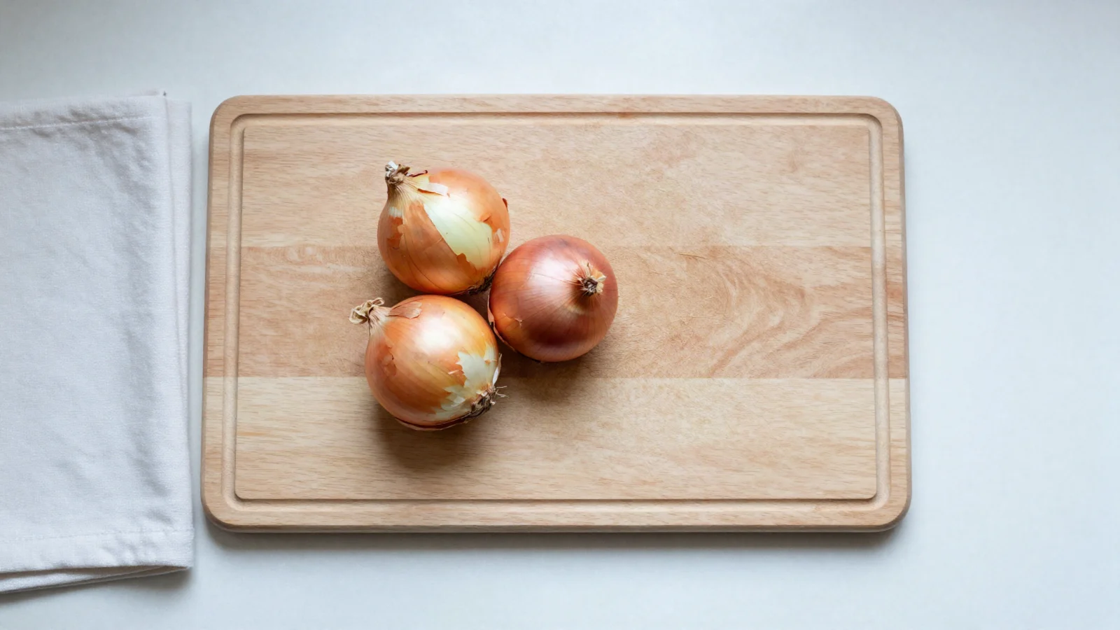 Three whole onions on a wooden cutting board.