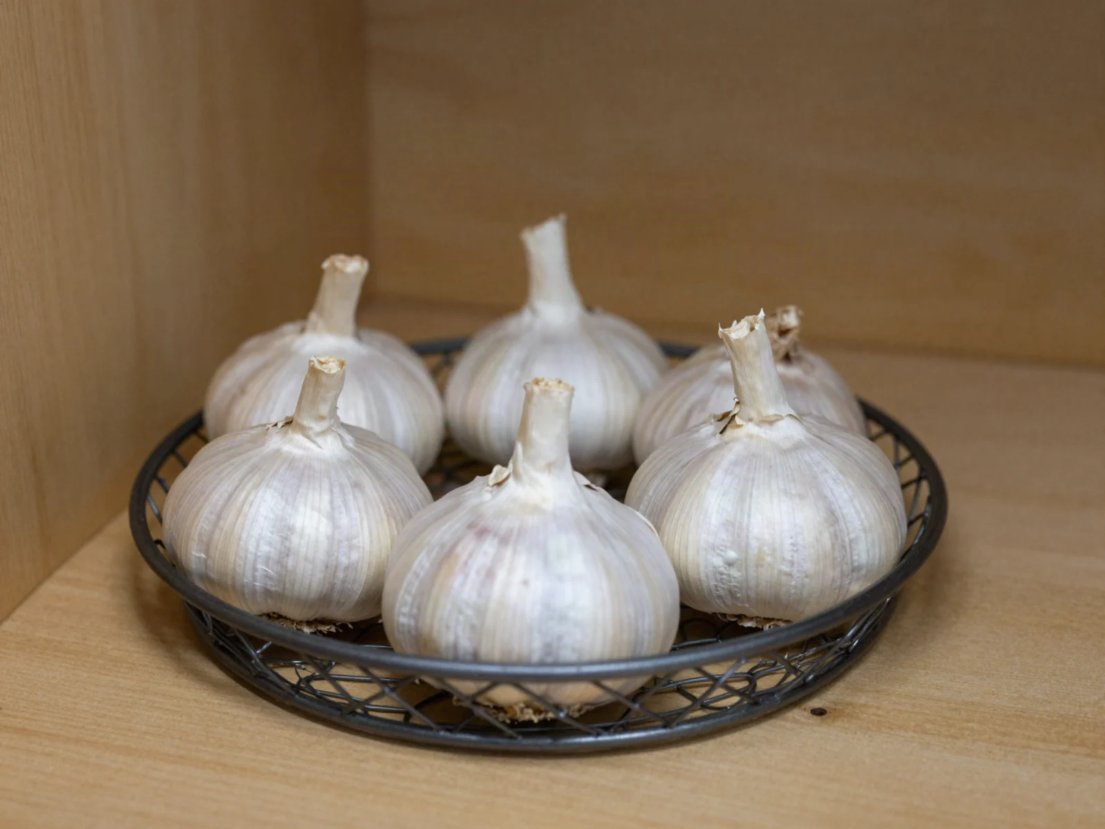 How to store garlic: whole bulbs in an open wire basket on a pantry shelf.