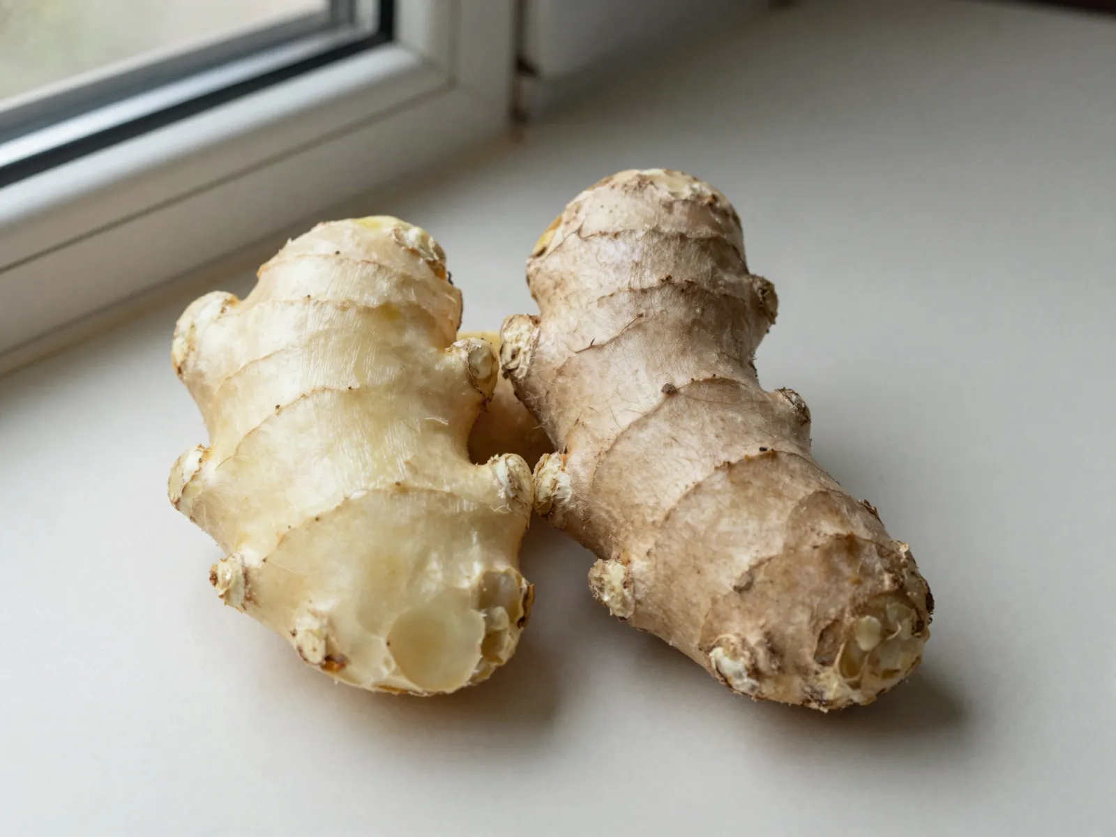 A pale, smooth fresh ginger root beside a duller, papery older root