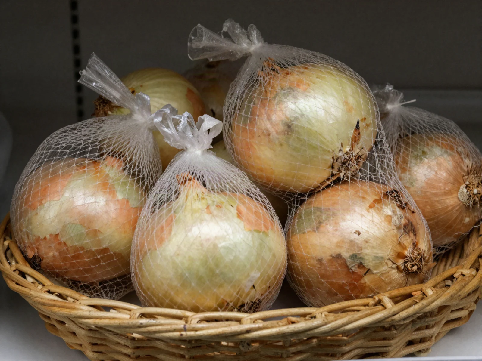 How to store onions: yellow onions in mesh bags in a wicker basket on a pantry shelf