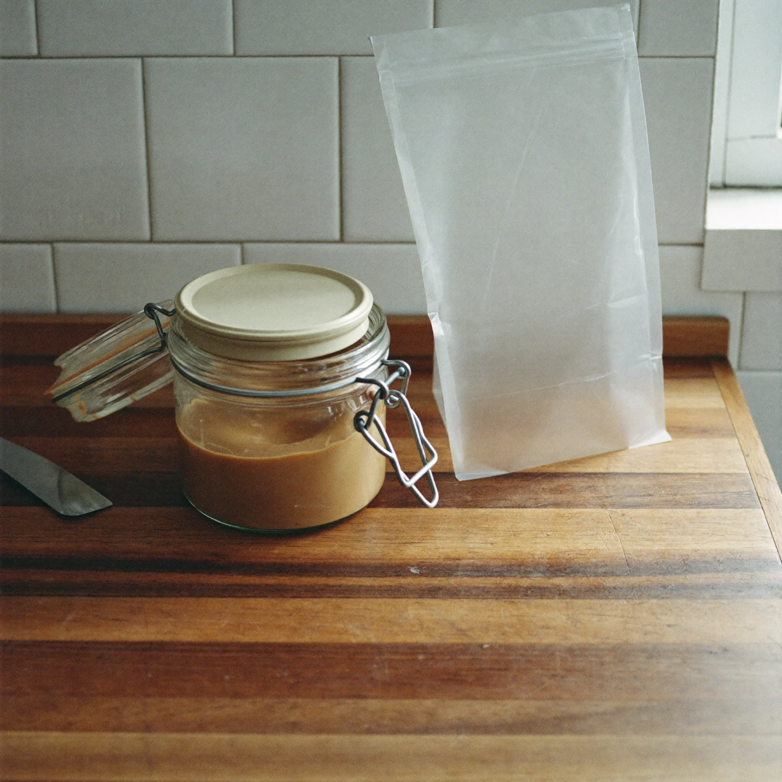 A sealed glass jar of stirred almond butter beside a freezer bag on the counter