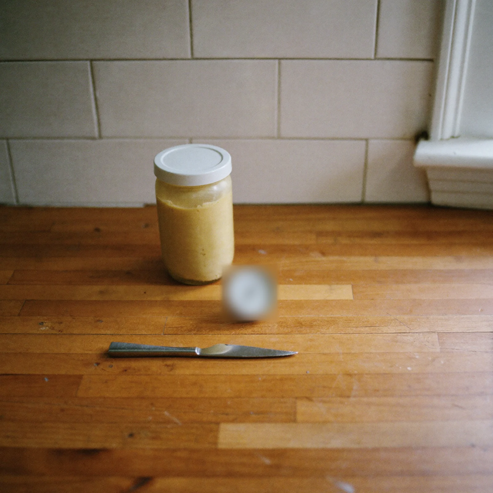 How to store almond butter: a lidded jar of almond butter beside a round dial fridge thermometer on a kitchen counter