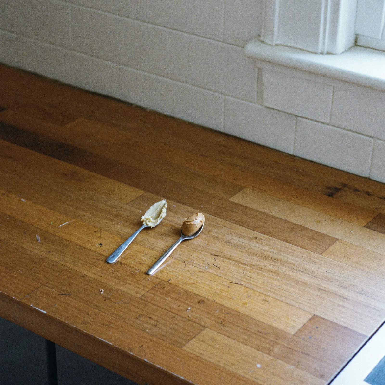 Two small spoons of almond butter compared on a counter, one pale and dull and one warmer brown