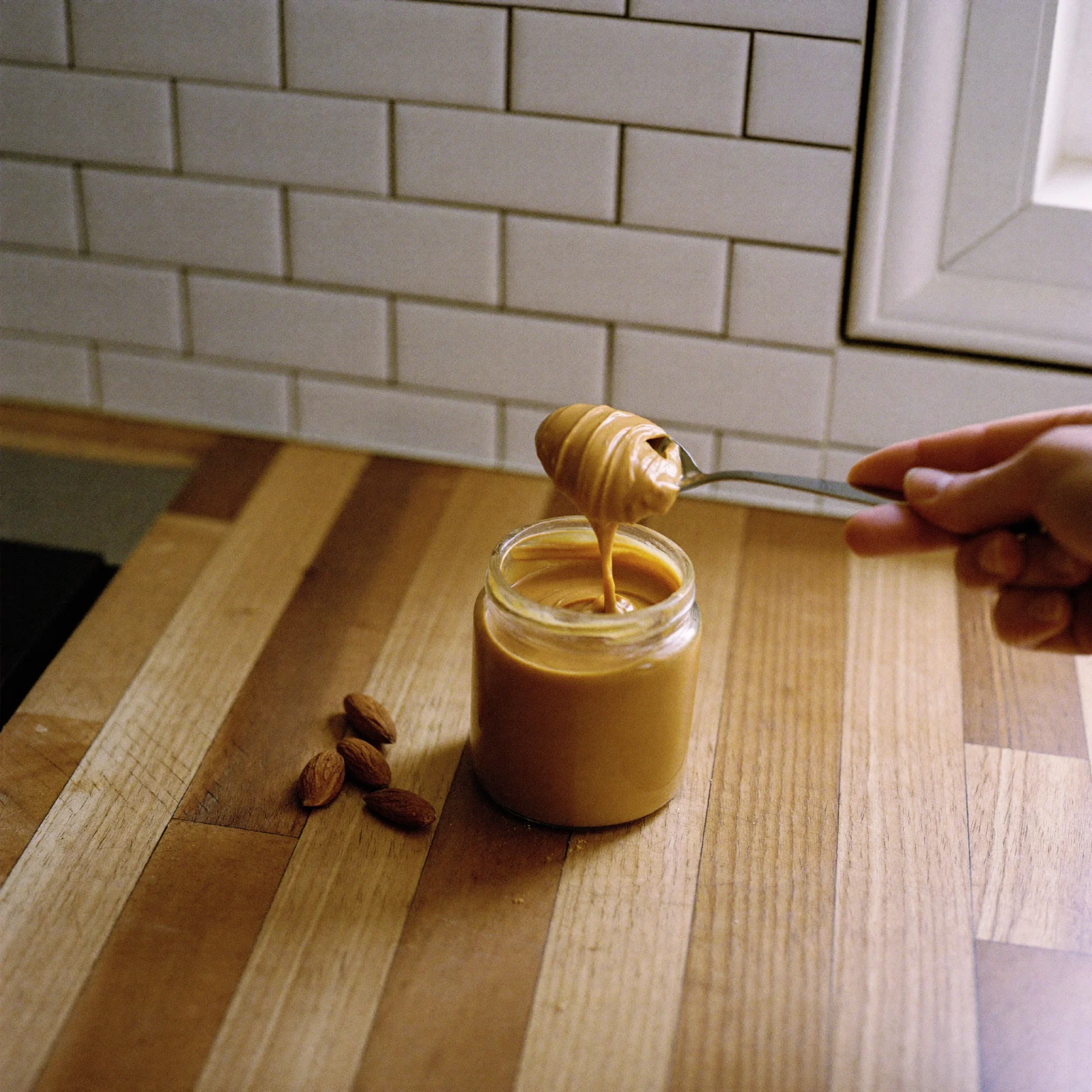A spoon lifting smooth, even light brown almond butter out of an open jar
