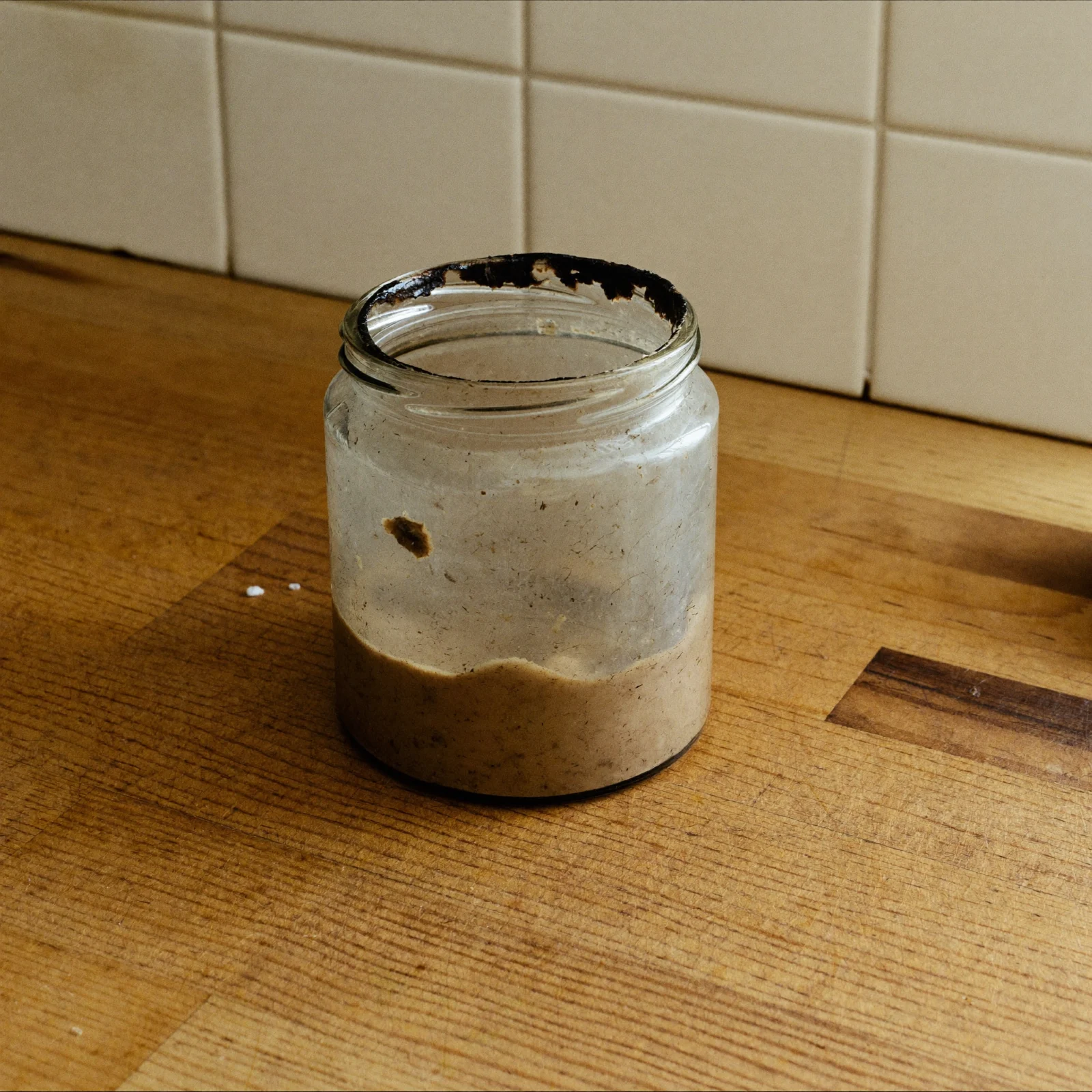 An open jar of almond butter gone dull and greyish brown at the surface with a darkened ring at the rim