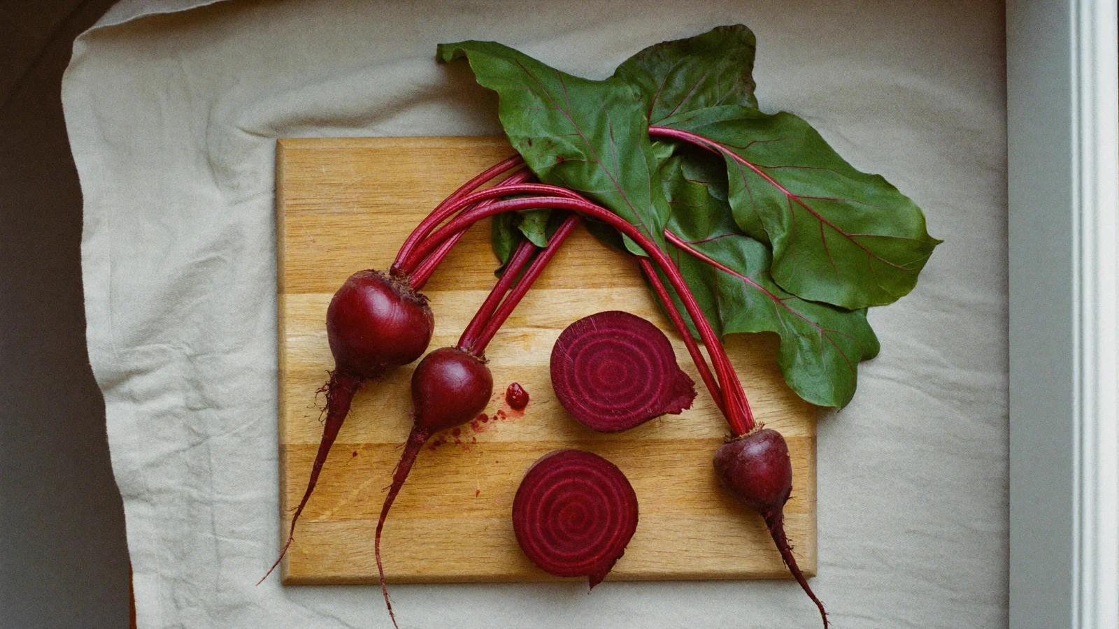 How to store Beets - Fresh red beets with their greens on a beech-wood board, one cut open to show the ringed purple flesh