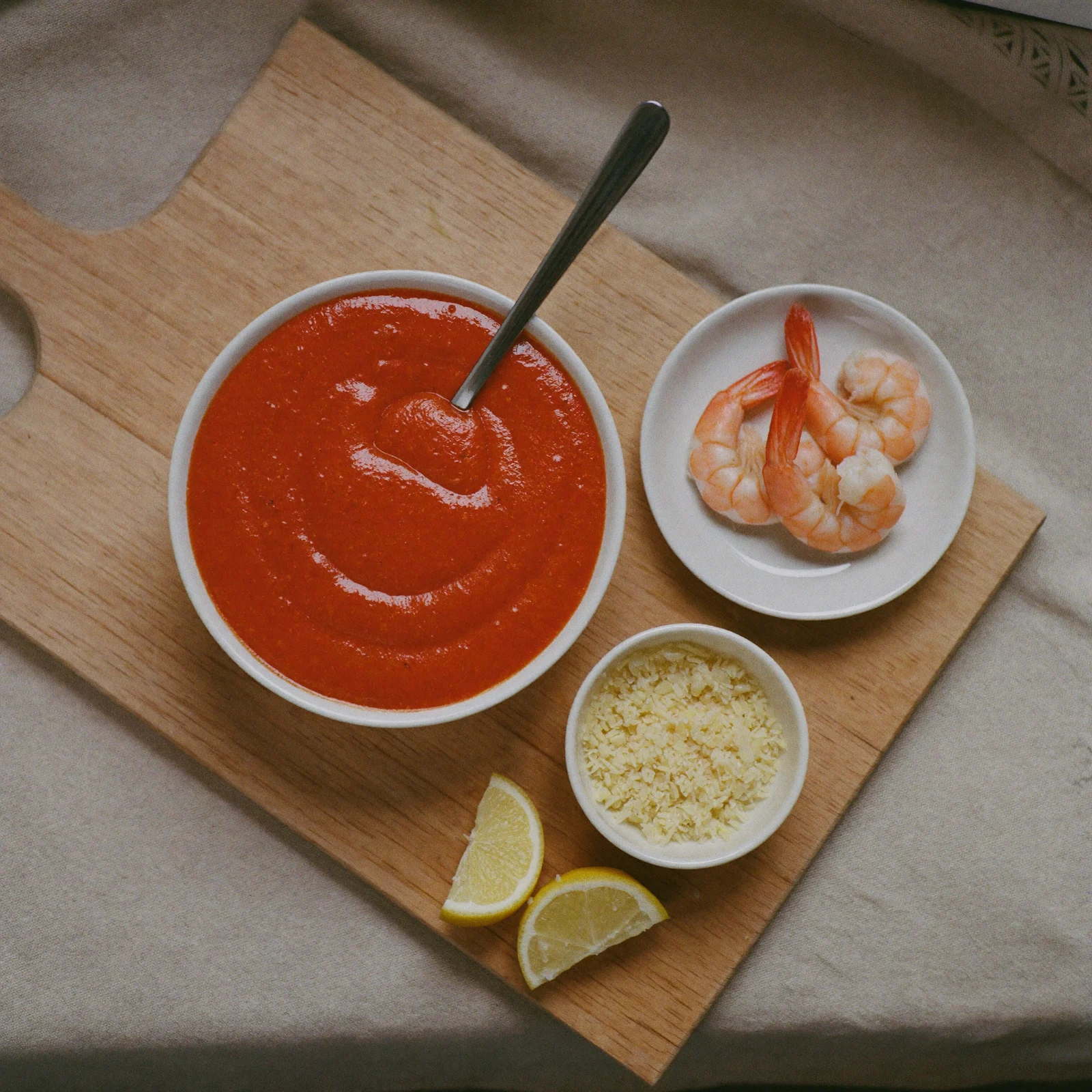 A bowl of cocktail sauce with shrimp, grated horseradish and lemon wedges on a beech-wood board