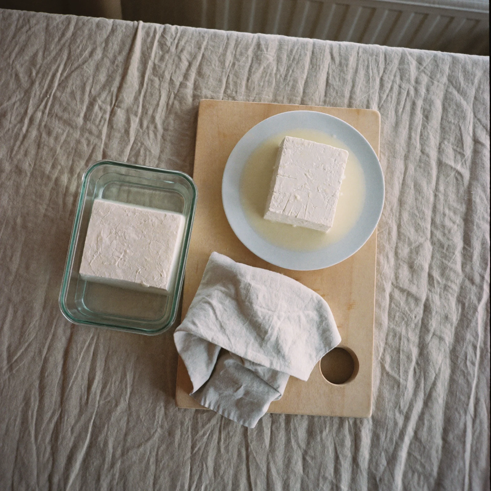 How to Store Tofu - a block of tofu on a plate and a second block in a glass container of water on a beech-wood board