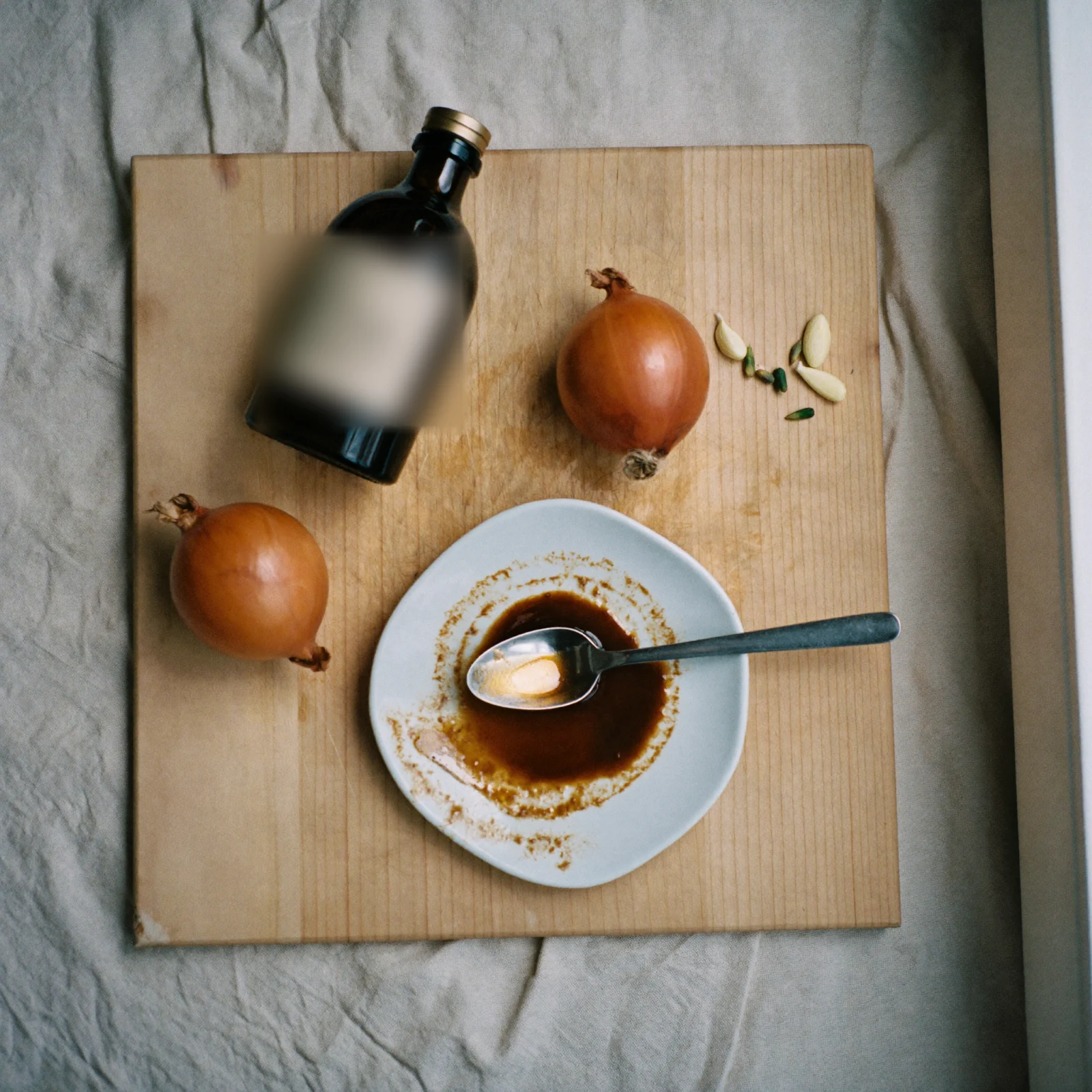 How to store Worcestershire sauce - a dark glass bottle of Worcestershire sauce on a beech-wood board beside onions, garlic and a dish of the poured sauce