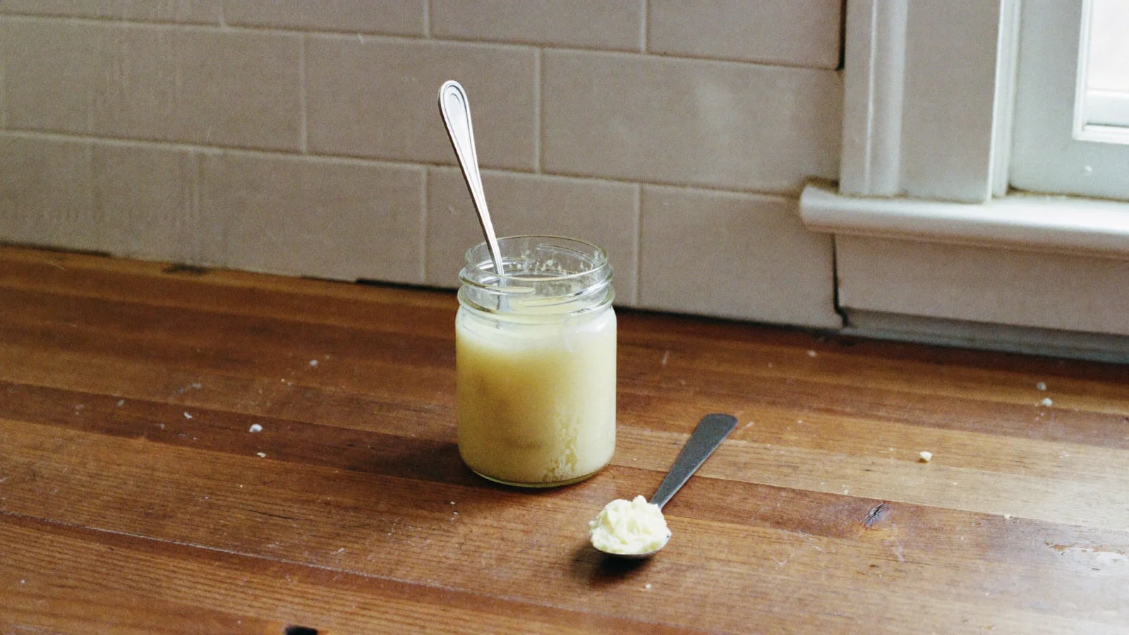 Honey set solid and pale in a jar with a spoon standing upright in it