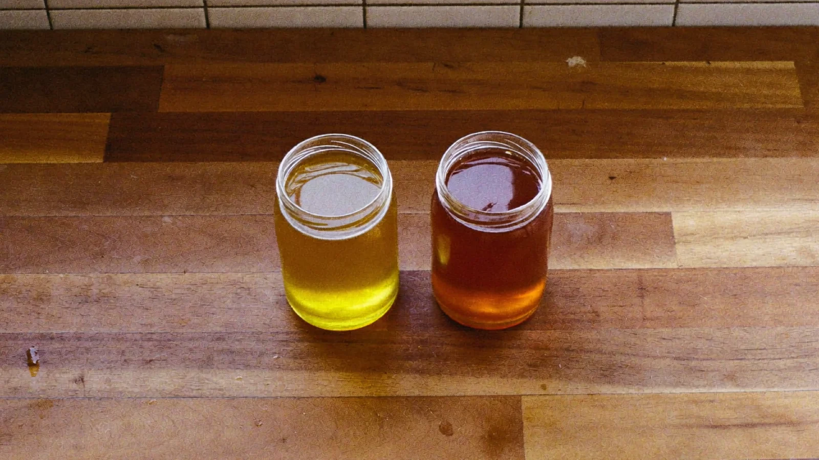 Two jars of honey side by side, one pale gold and one much darker amber
