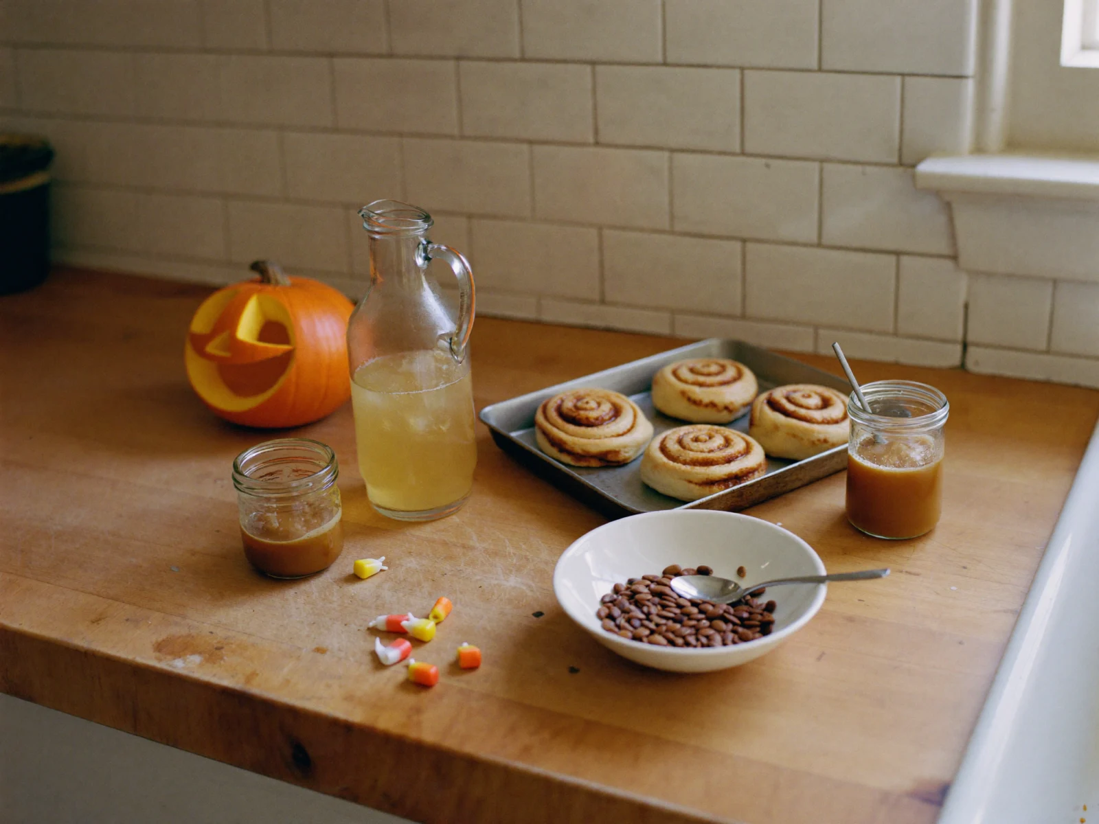 How to Store Halloween Leftovers - Halloween leftovers on a kitchen counter: a carved jack-o'-lantern, a jug of apple cider, a tray of cinnamon rolls, two jars of caramel sauce and a few pieces of candy corn