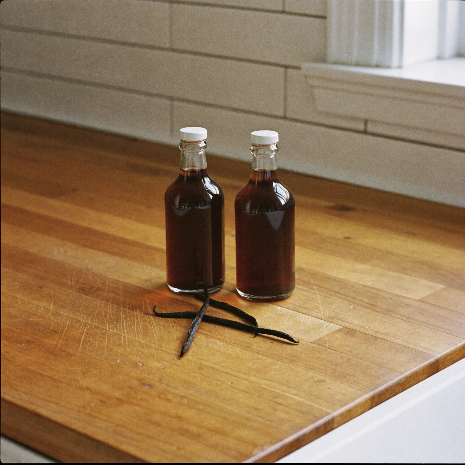 Two plain bottles of vanilla side by side, with whole vanilla beans in front of one