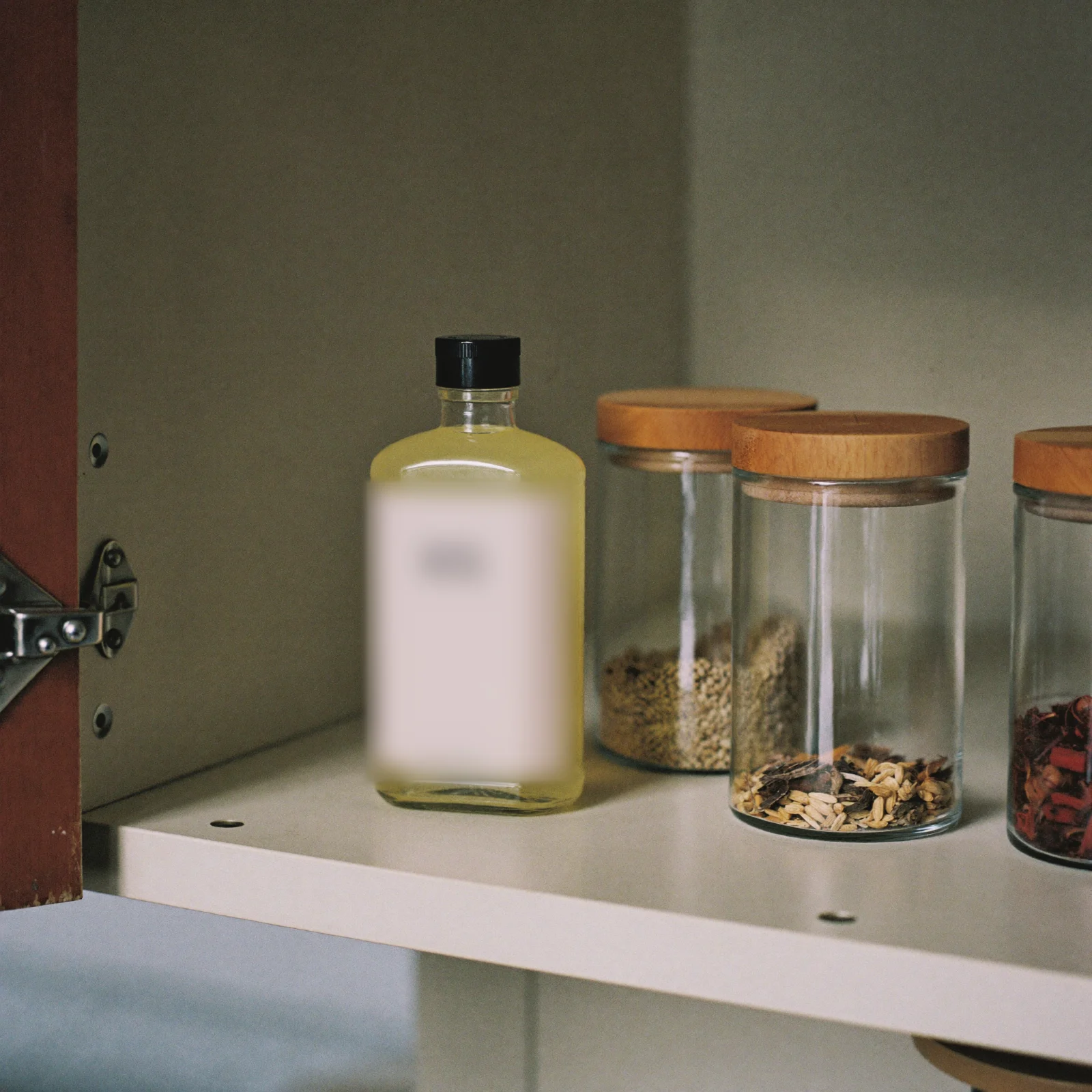 A bottle of lemon extract standing upright on a cupboard shelf beside jars of dried spices