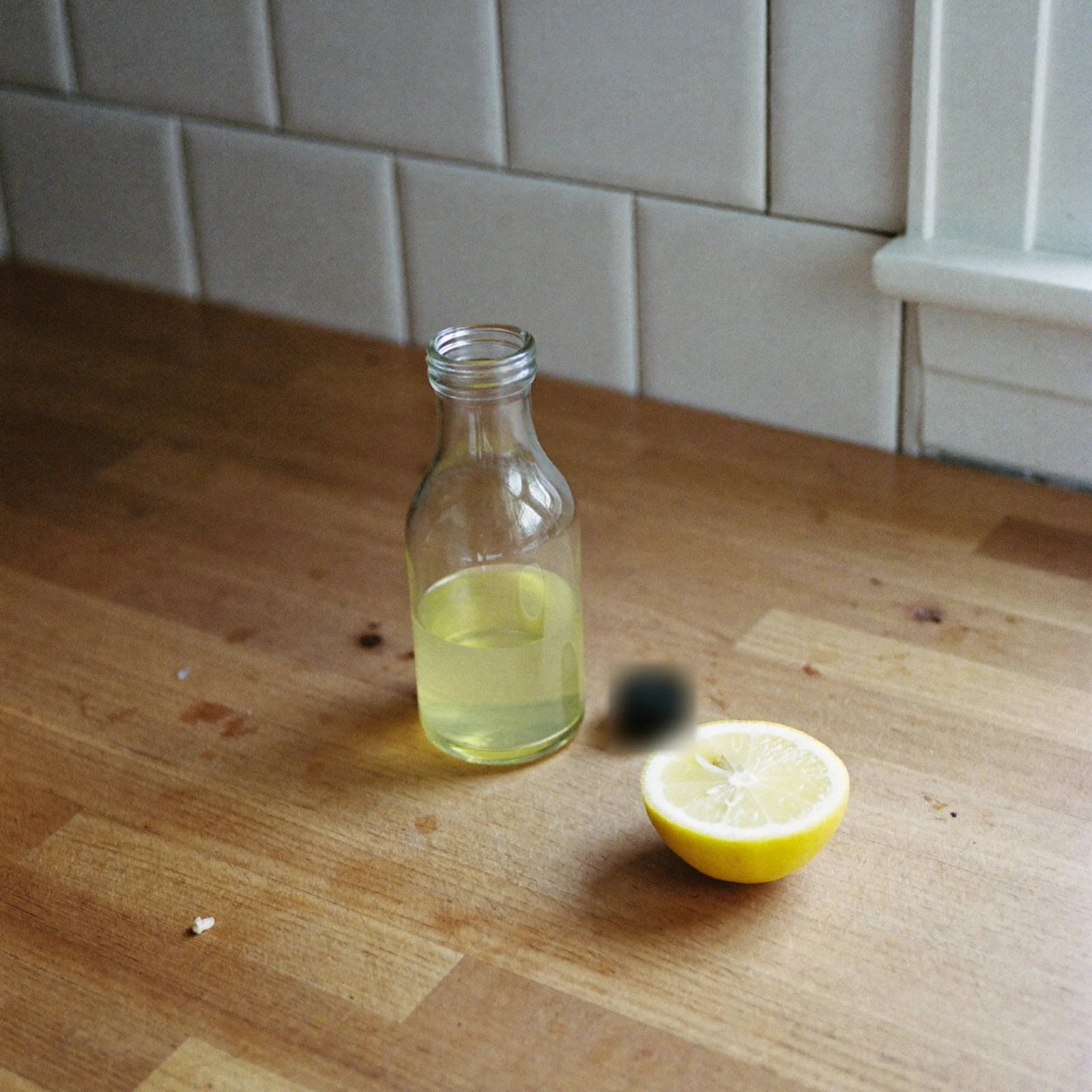 A half-full bottle of pale yellow lemon extract with its cap off beside a lemon half