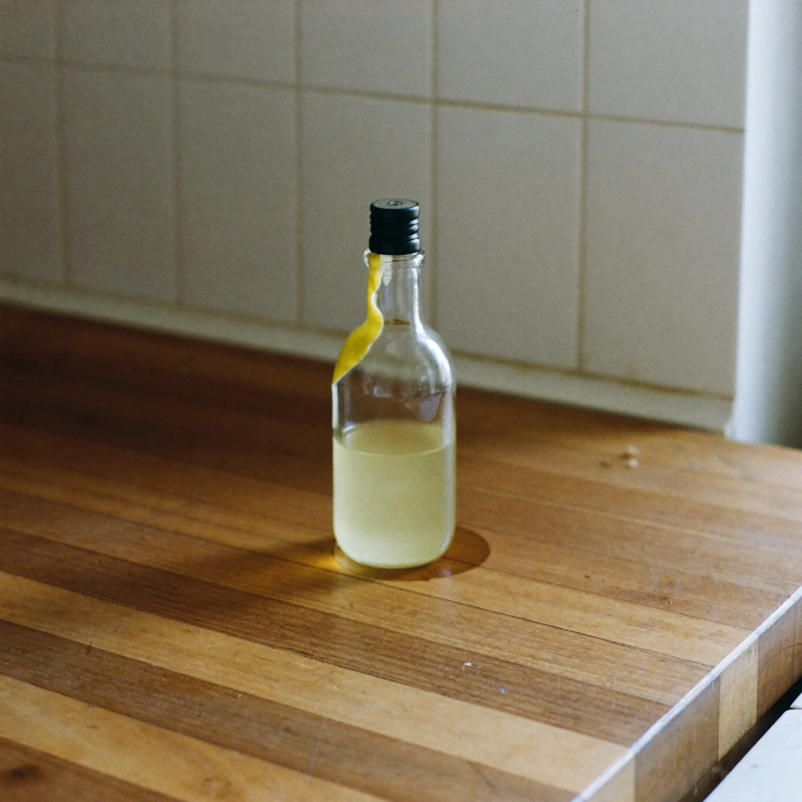 A bottle of lemon extract with a sticky streak running down its neck and a ring stain on the counter beneath it