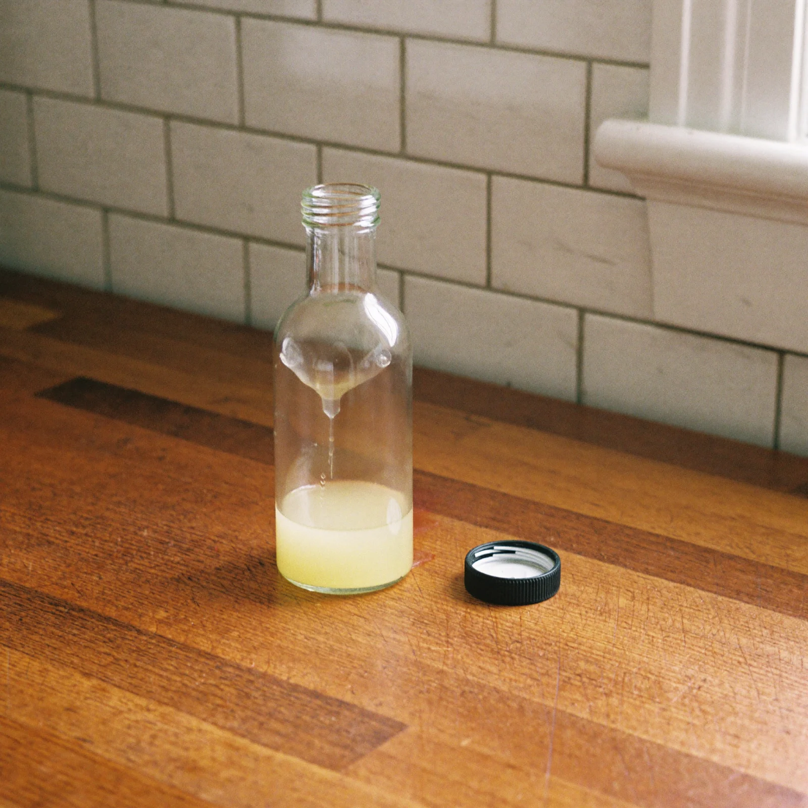 A bottle of lemon extract filled only a third of the way up, with its cap sitting loose beside it