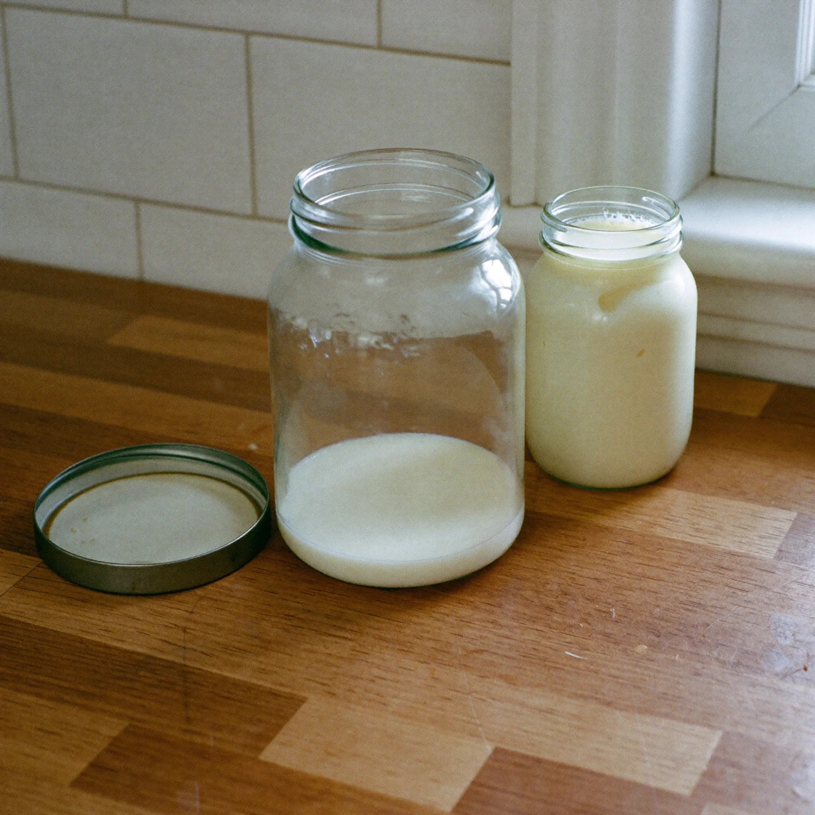 A glass jar of milk with plenty of headspace beside a jar of frozen milk