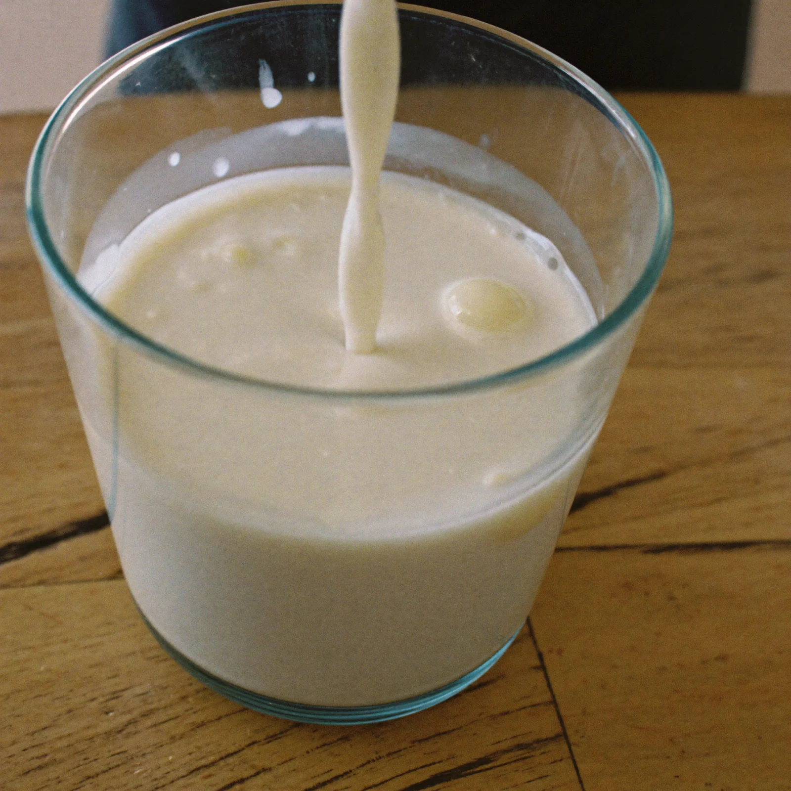 Thick, lumpy milk with small curds being poured into a glass