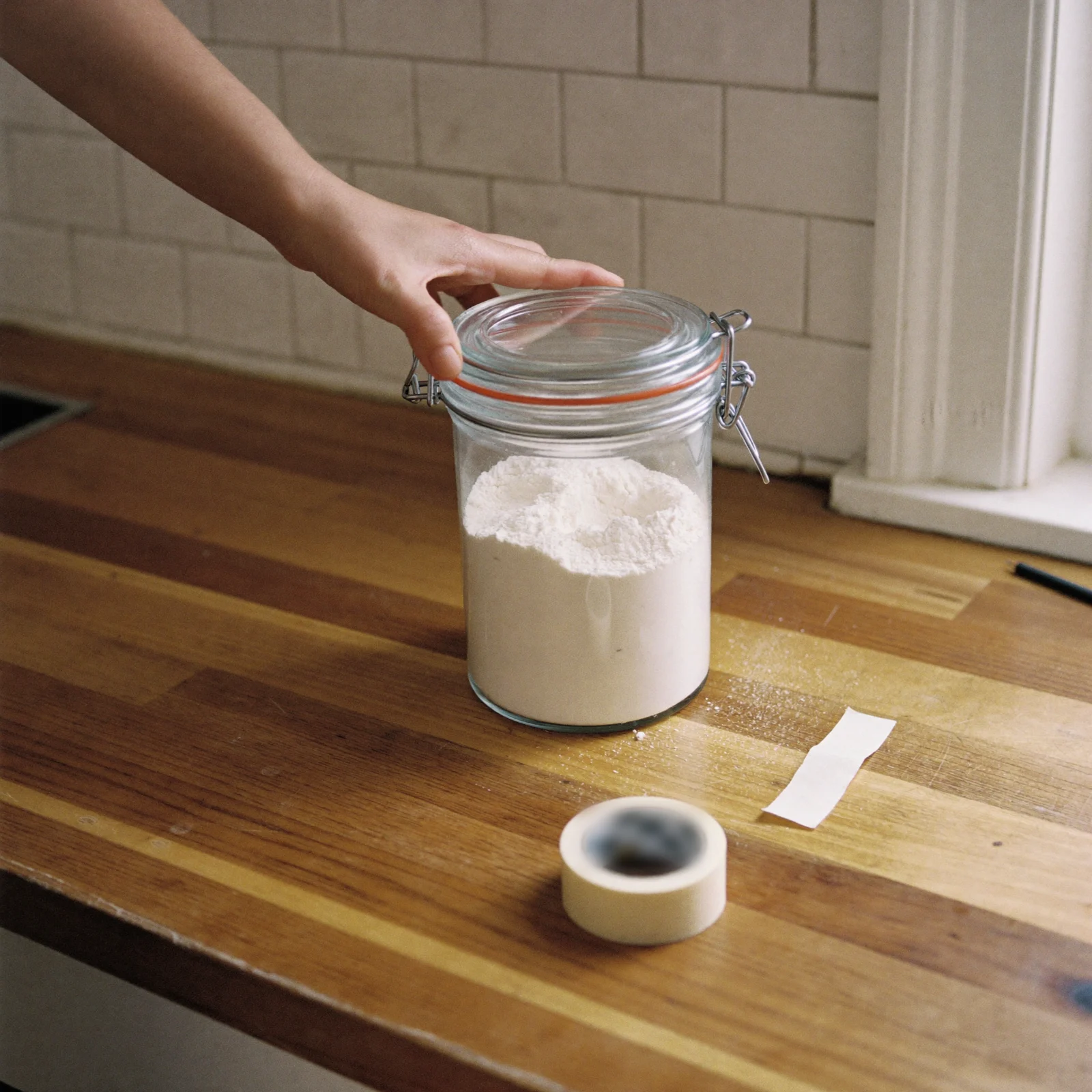 Sealing self-rising flour in an airtight glass canister, with tape ready to mark the date