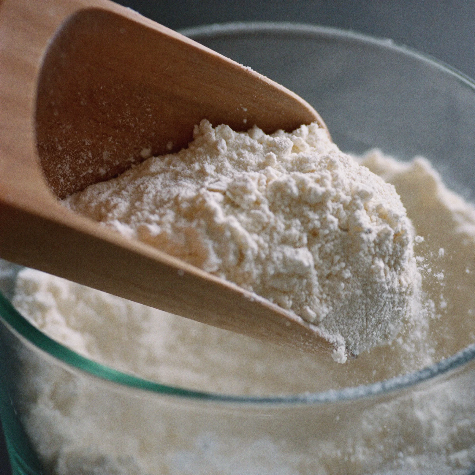 A scoop of fresh, loose white self-rising flour lifted from a glass canister