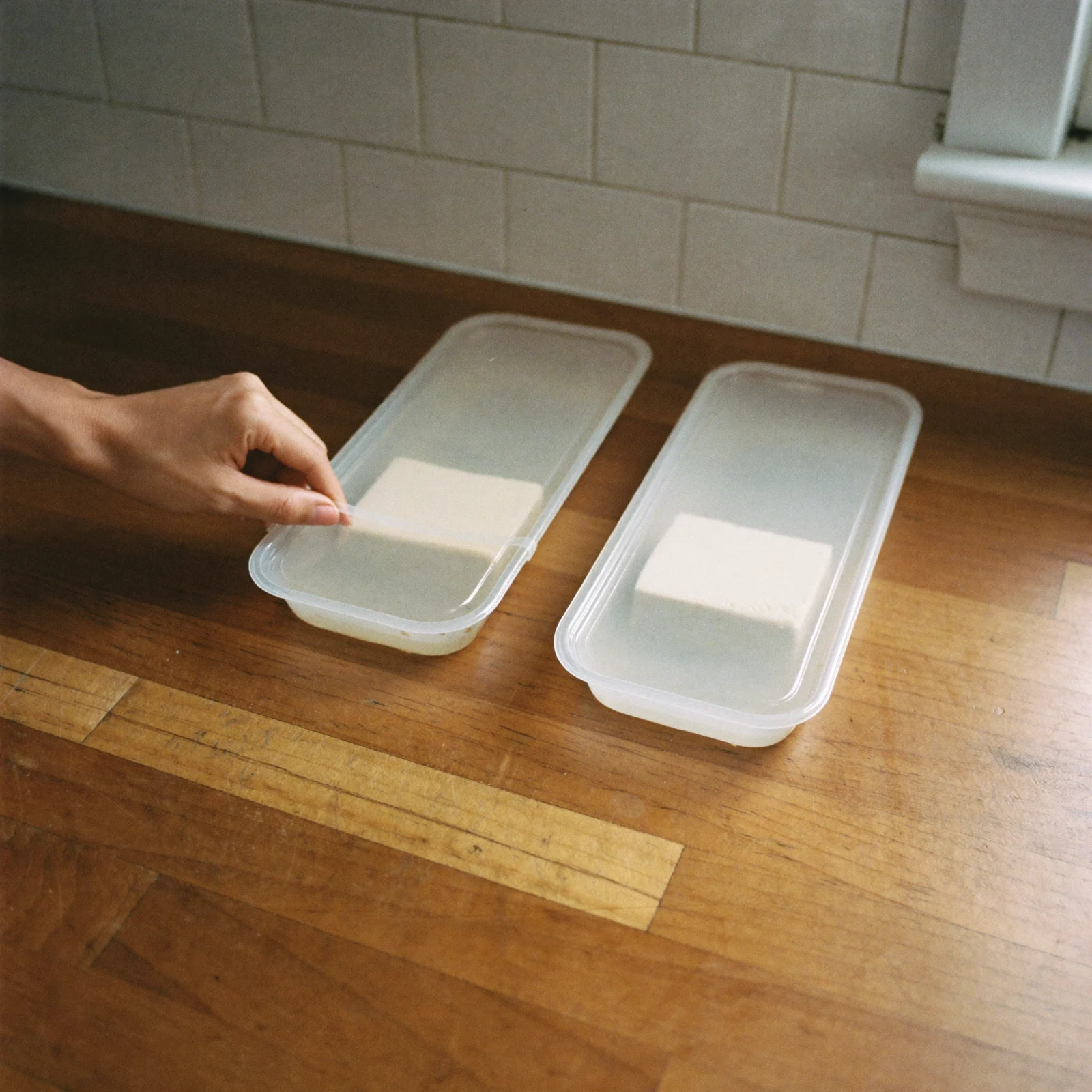 Two plain sealed tubs of water-packed tofu on a counter before buying