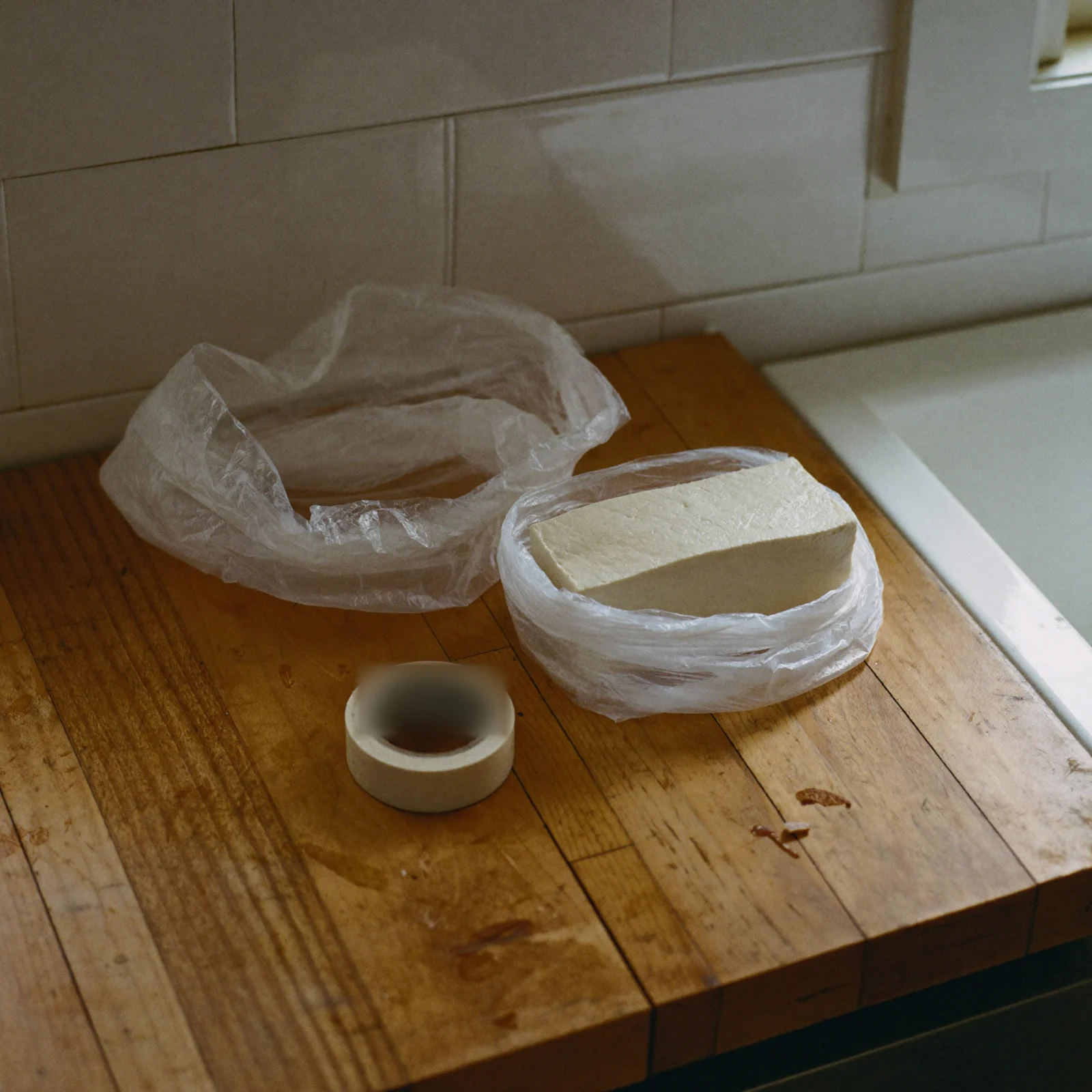 A drained block of tofu wrapped in plastic for the freezer, beside a roll of masking tape