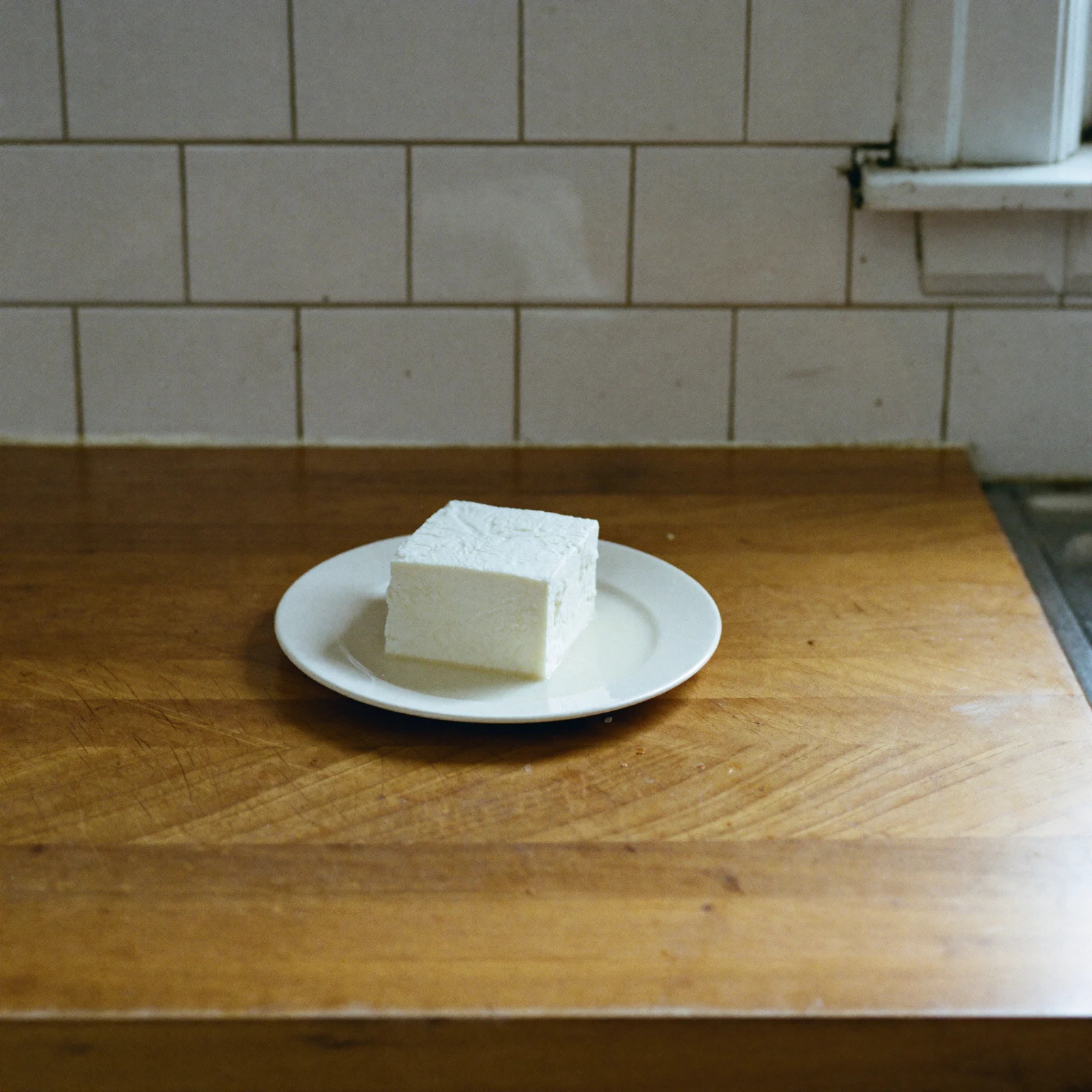 A fresh block of tofu, creamy white and firm, on a white plate