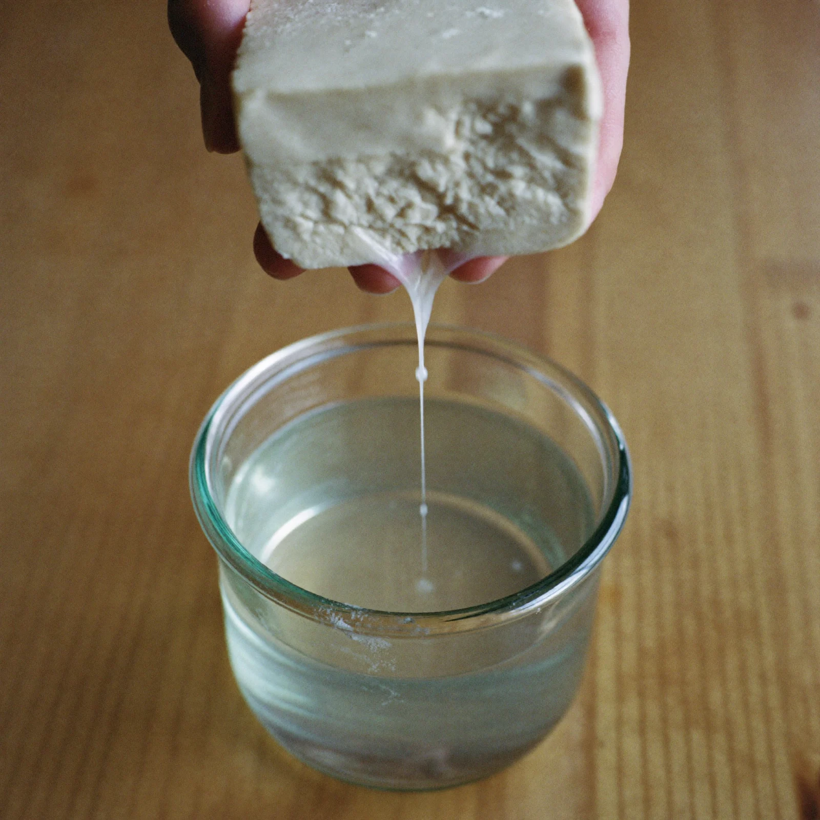 A block of tofu with a slippery film on its surface, lifted from the container