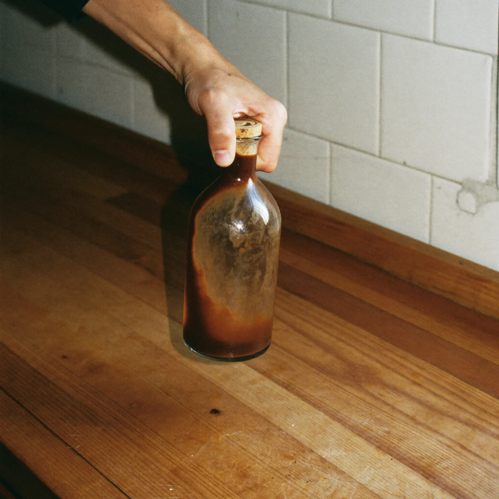 A hand holding a corked bottle of Worcestershire sauce with sediment clouding the glass