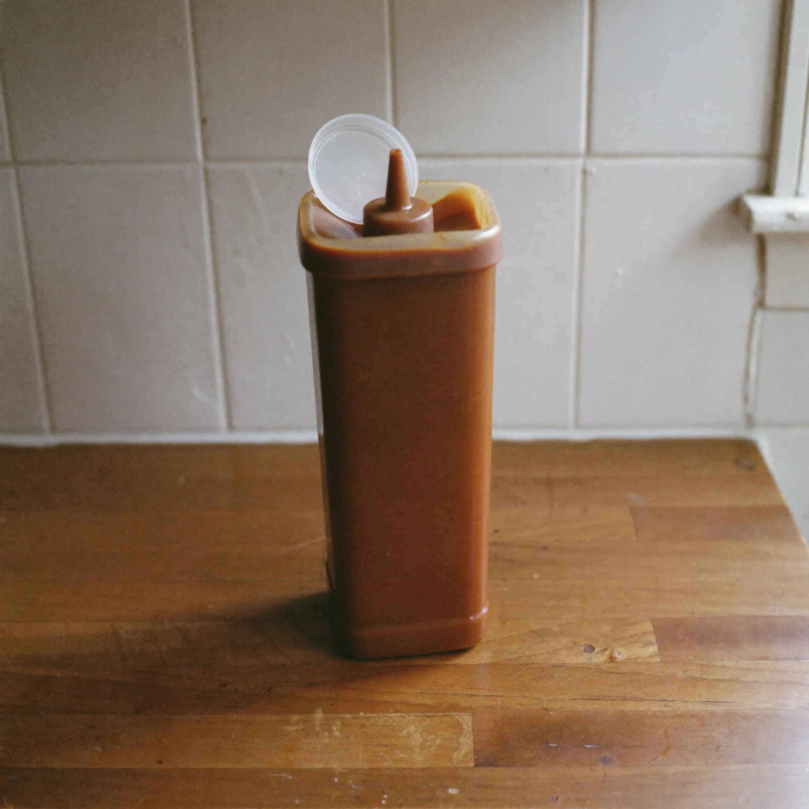 A plastic squeeze bottle of brown sauce with its cap flipped open on the counter