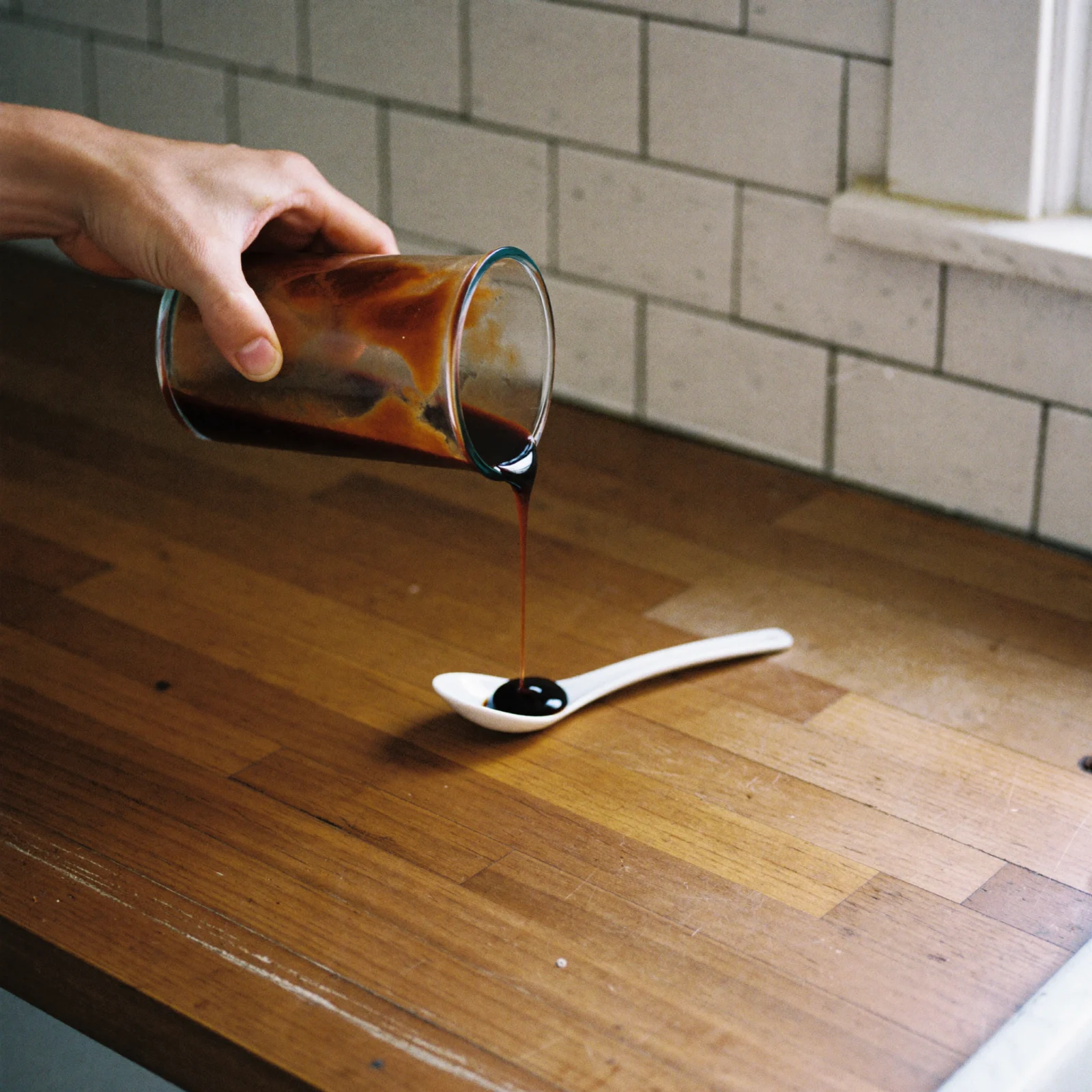 Dark Worcestershire sauce pouring in a thin stream into a white spoon